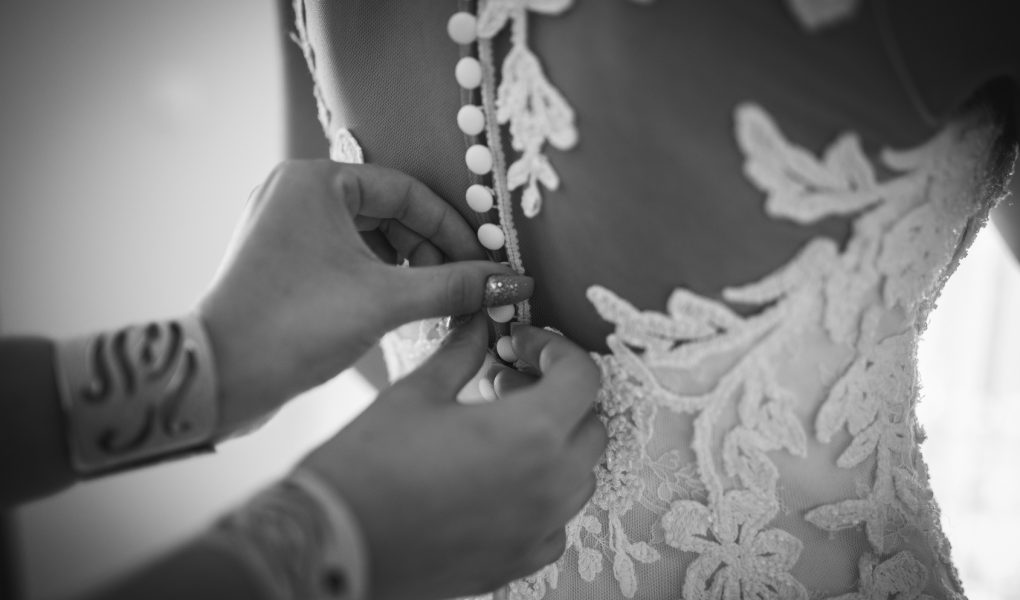 Une demoiselle d'honneur ajuste la robe de la mariée lors de l'essayage